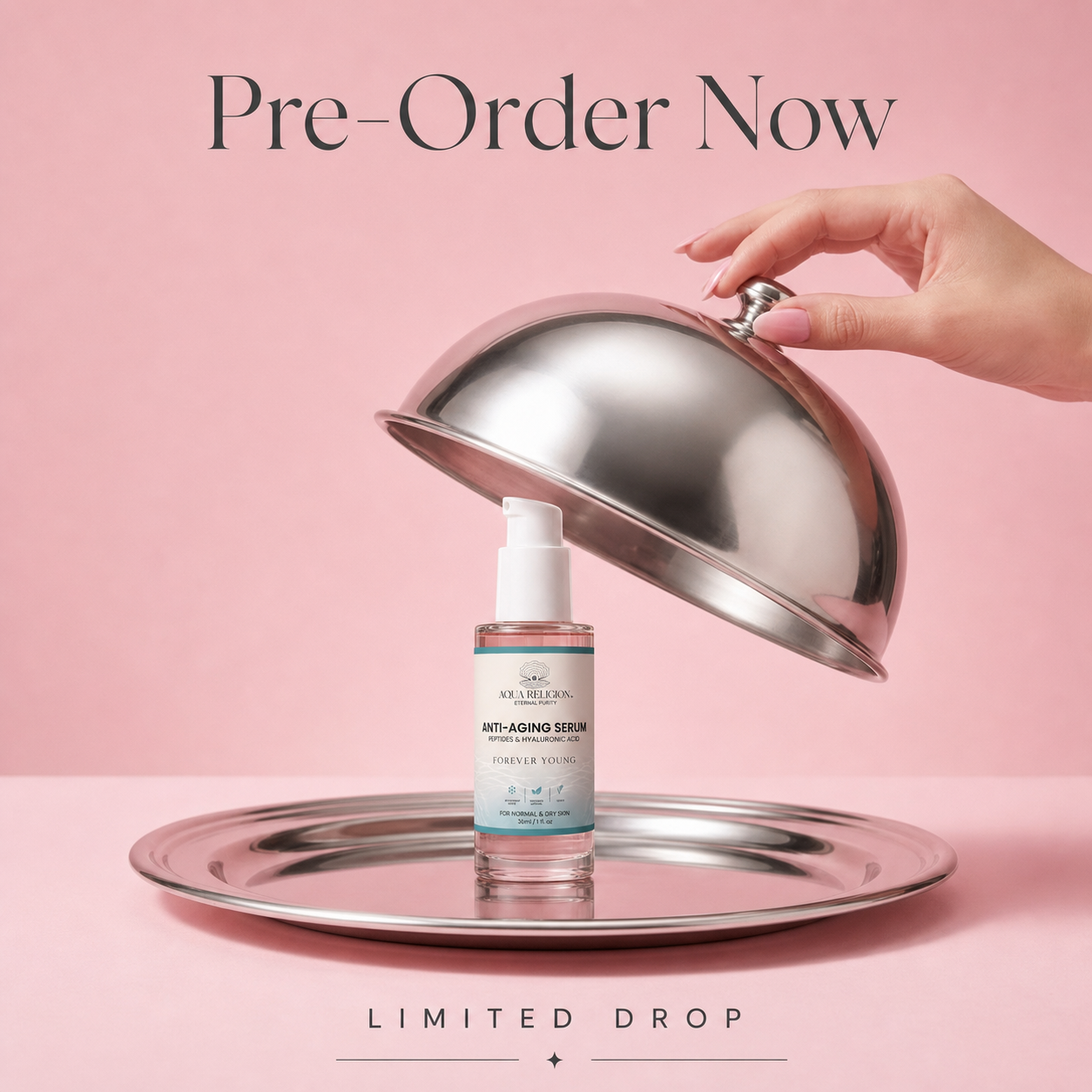 A hand lifts a shiny silver cloche to reveal a small skincare serum bottle on a matching silver tray against a soft pink background. Text at the top reads 'Pre-Order Now' and text at the bottom reads 'LIMITED DROP'.